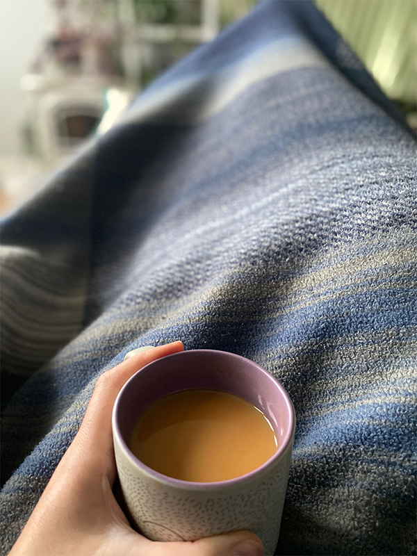 Photograph of Sarah Scott life coach  sitting under a blanket holding a cup of tea. The blanket is blue and the background is blurred.