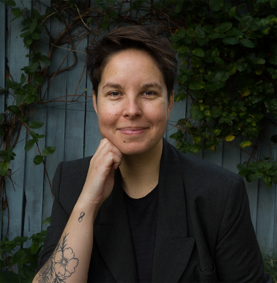 Photograph of Sarah Scott life coach in front of a blue-grey fence and a climbing shrub.